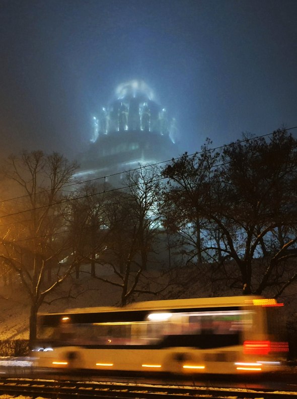 'Ghosts' by Charlotte Waygood. A bus speeds past an illuminated military memorial appearing out of the fog