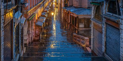 View down wet pathway between buildings, with light shining off wet paving - Intellectual and Cultural History