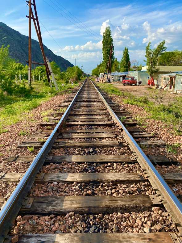 'Trackside in Uchuruk' by Barney Crawford. A view down a railway track with buildings, hills and trees either side