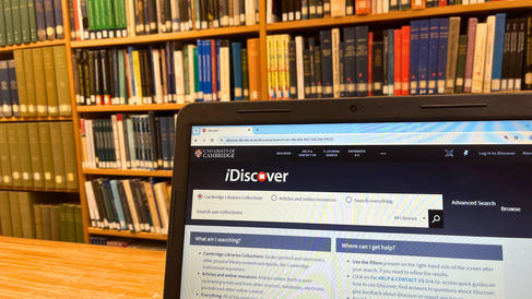 A shared desk in the French section of the MMLL Library. A laptop is showing the iDiscover homepage.