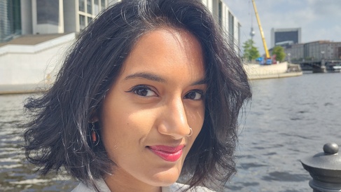 woman with black hair in front of river with modern buildings in background