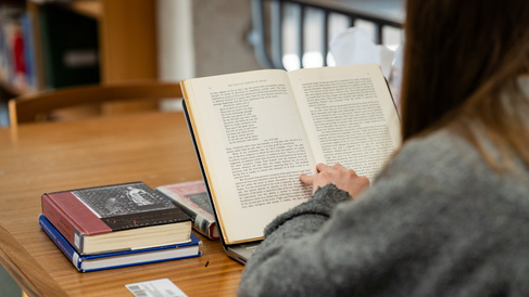 Student reading a book on Chrétien de Troyes in the MMLL Library.