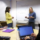 Video still showing an academic in front of a whiteboard talking to three students