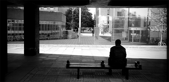 Black and white photo of person sitting on a bench outside the Raised Faculty Building