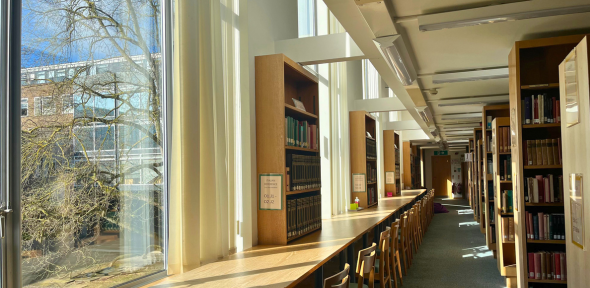 A long row of desks and chairs in the MMLL Library, next to the Spanish Section, looking out over the grass in the middle of the Raised Faculty Building.